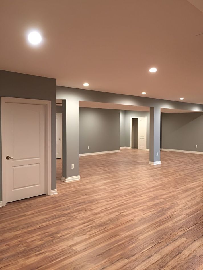 Empty finished basement with wood-look flooring, gray walls, white doors, and recessed ceiling lights.