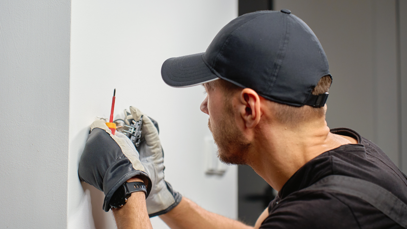 Technician in cap and gloves measuring a wall with a pencil and tape measure.