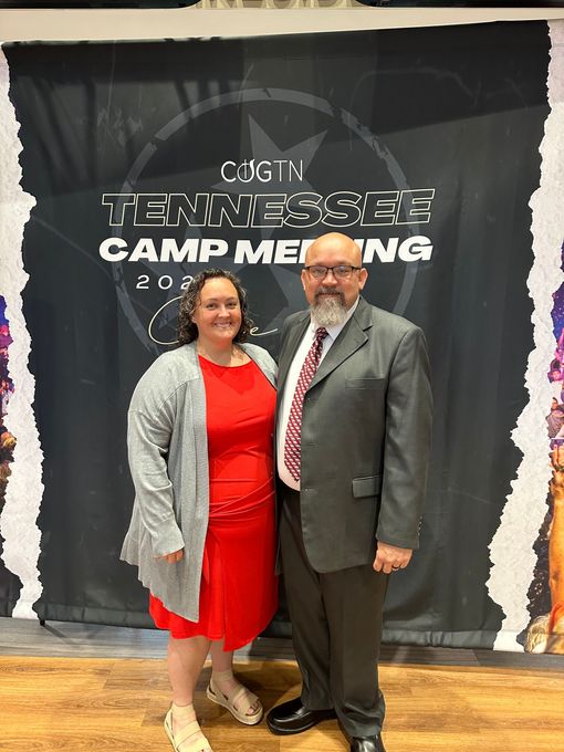 A man and a woman are posing for a picture in front of a tennessee camp meeting banner.