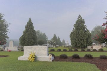 Graveyard with white headstones, green lawns, and tall trees under a hazy sky.