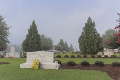 Graveyard with white headstones, green lawns, and tall trees under a hazy sky.