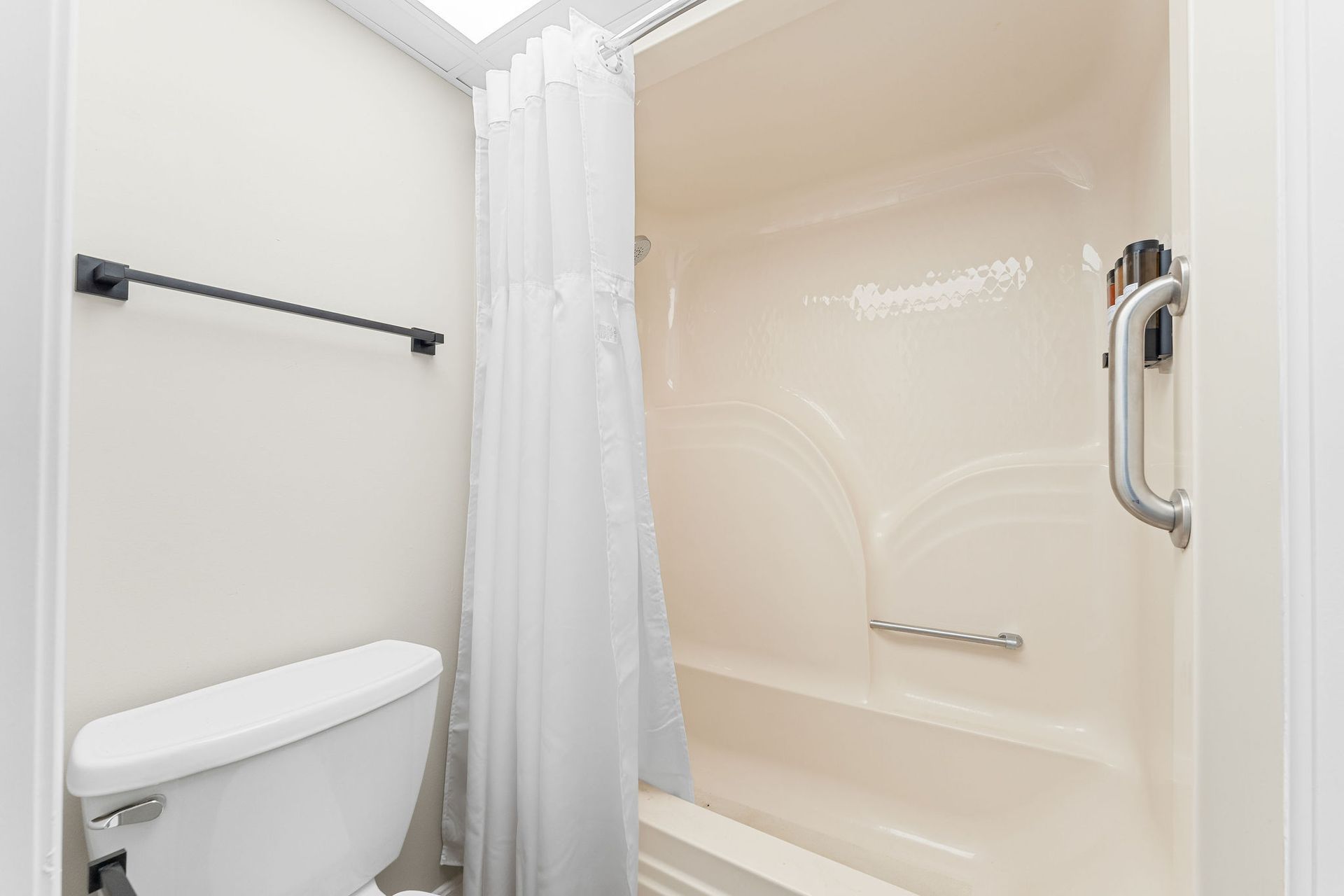 A bathroom interior featuring a white toilet, a towel rack, and a shower-tub combo with a white curtain and grab bar.