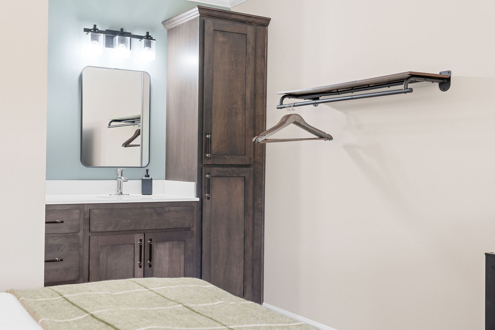 A bedroom corner features a vanity with dark wood cabinets, a mirror, and a wall-mounted metal clothes rack with a hanger.