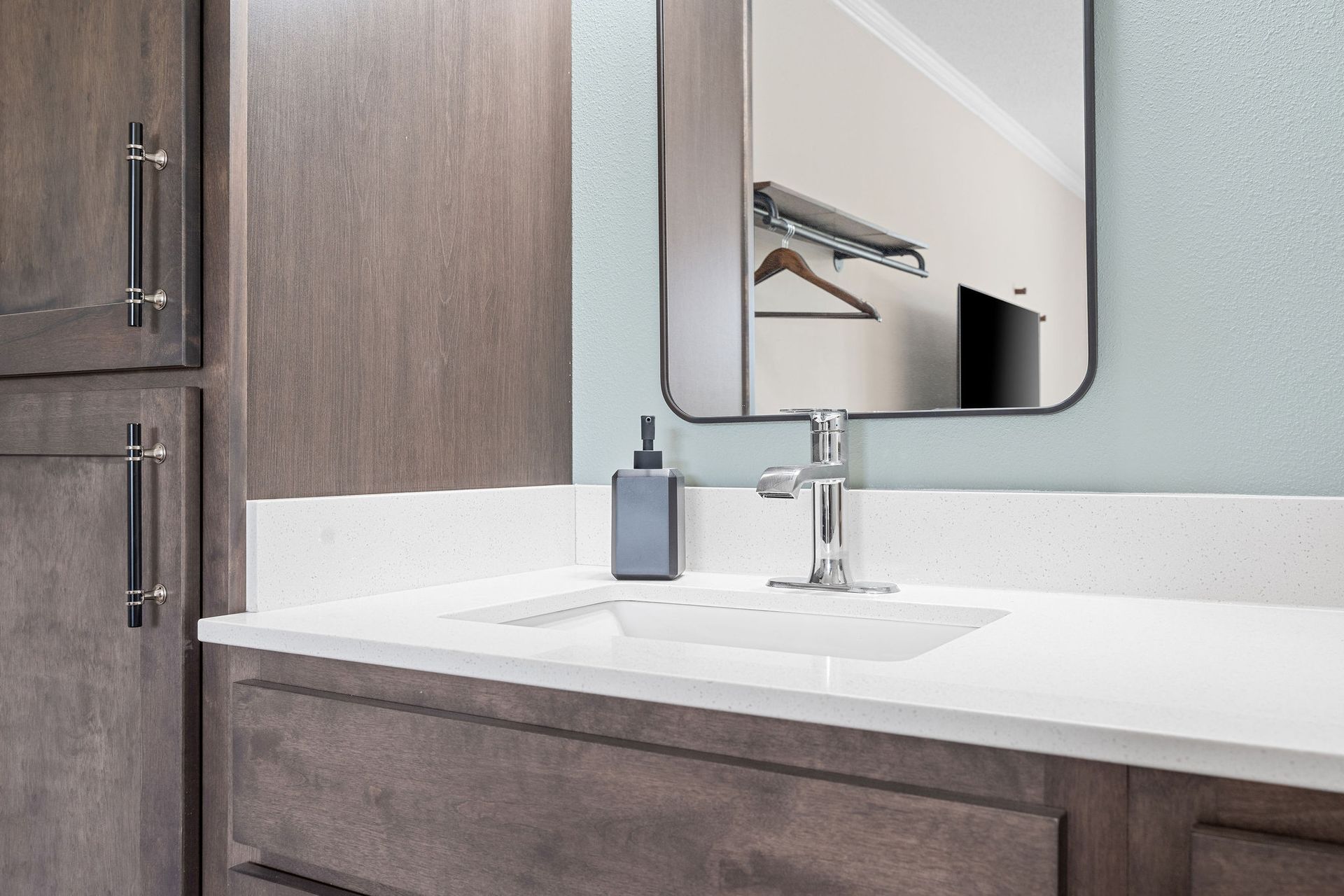 A bathroom vanity with a white countertop, modern silver faucet, grey soap dispenser, and a wall mirror.