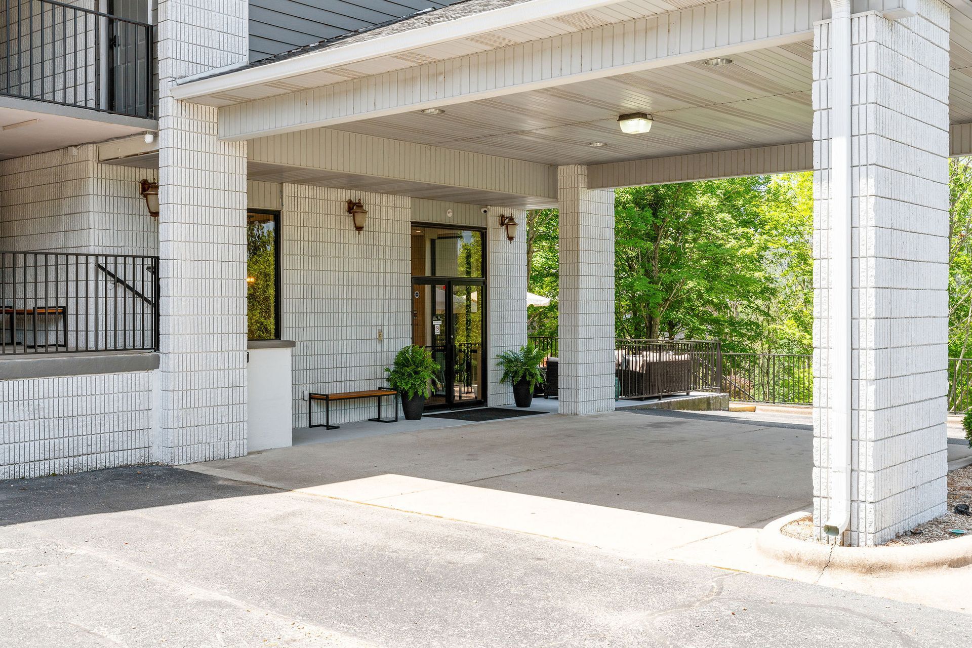 Entrance to a building with a white brick facade and covered porte-cochère, featuring glass doors and potted plants.