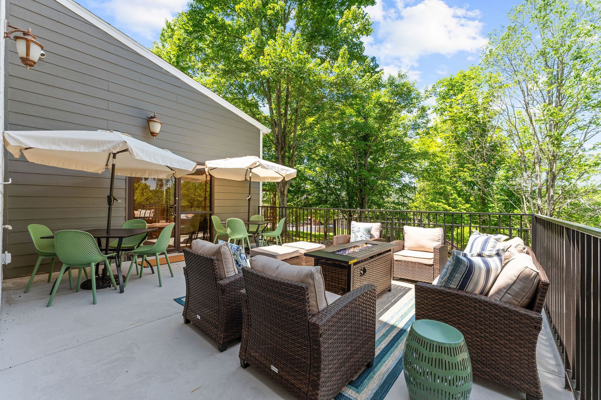 A spacious deck with wicker patio furniture, umbrellas, and a dining set, overlooking a lush green forest.