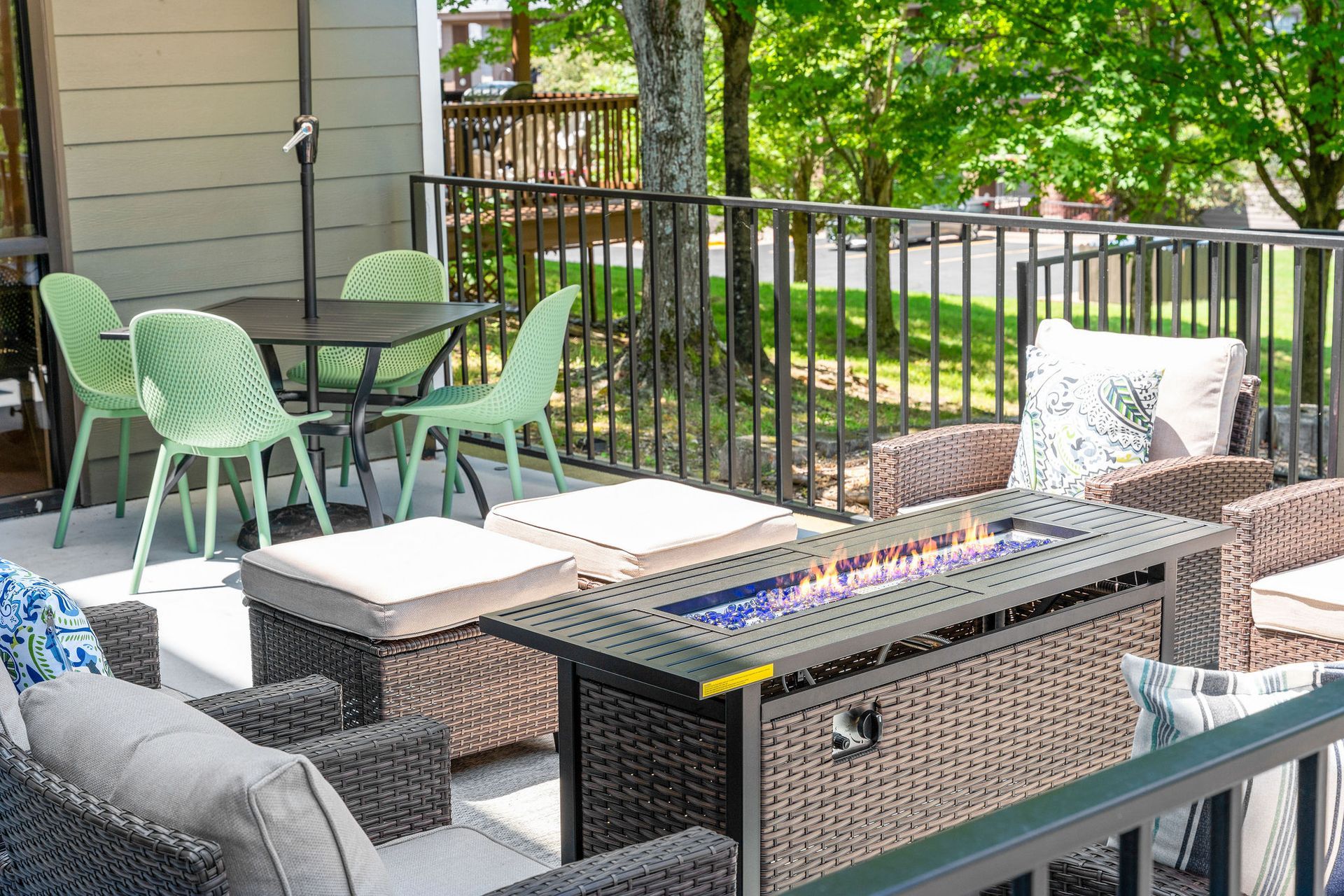 A patio with a lit fire pit table, wicker furniture, and a separate dining set with light green chairs on a deck.
