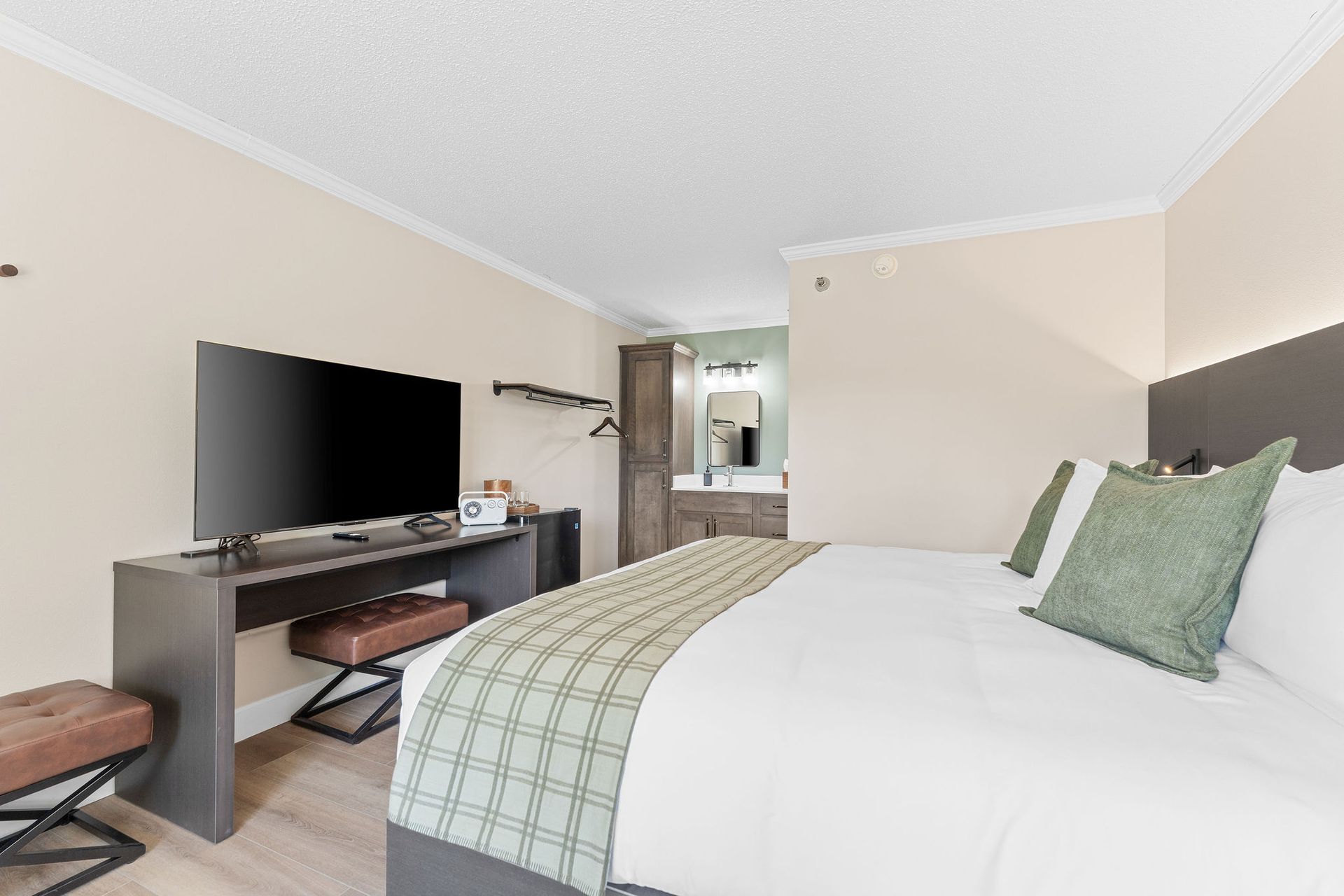 A hotel room featuring a bed with white bedding, a desk with a television, and a doorway leading to a bathroom.