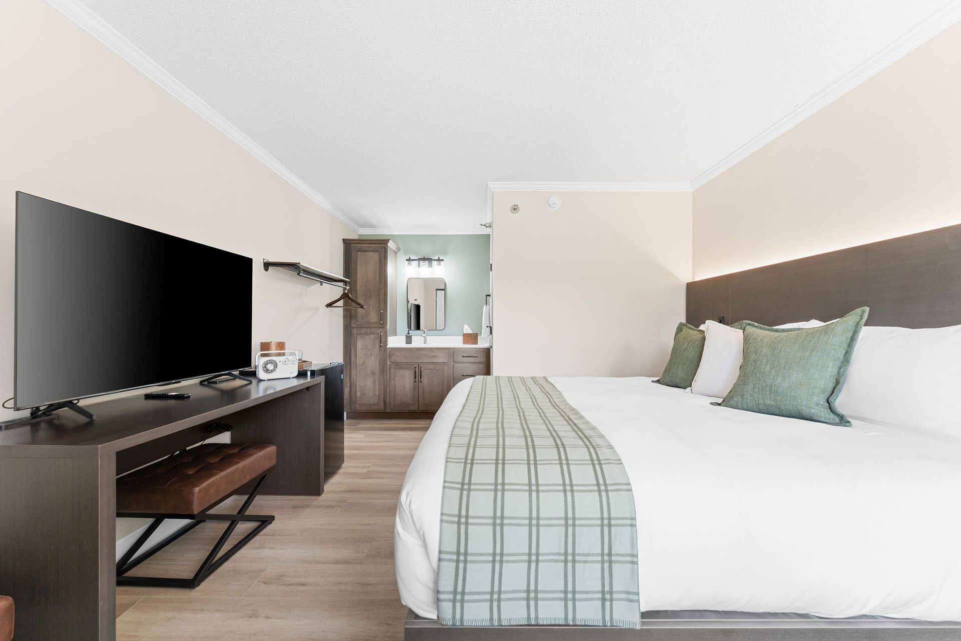 A hotel room with a large bed, a desk area with a flat-screen TV, and an open view into the bathroom.