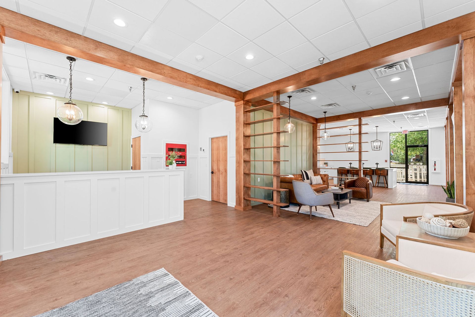 A bright, modern lobby with a white reception desk, light wood-look flooring, and a cozy seating area with armchairs.