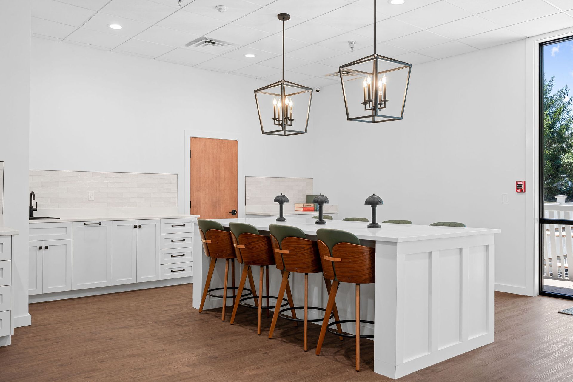 A modern, minimalist lobby featuring a white kitchen island with bar stools, pendant lighting, and clean, white cabinetry.