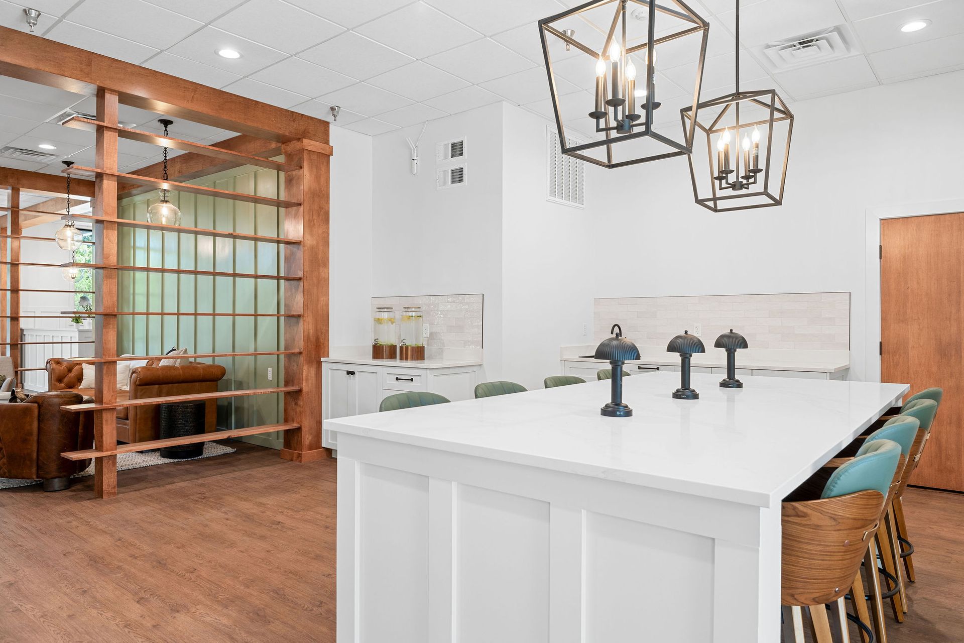 A modern office kitchen area featuring a white quartz island with three black stools and two hanging lantern lights.