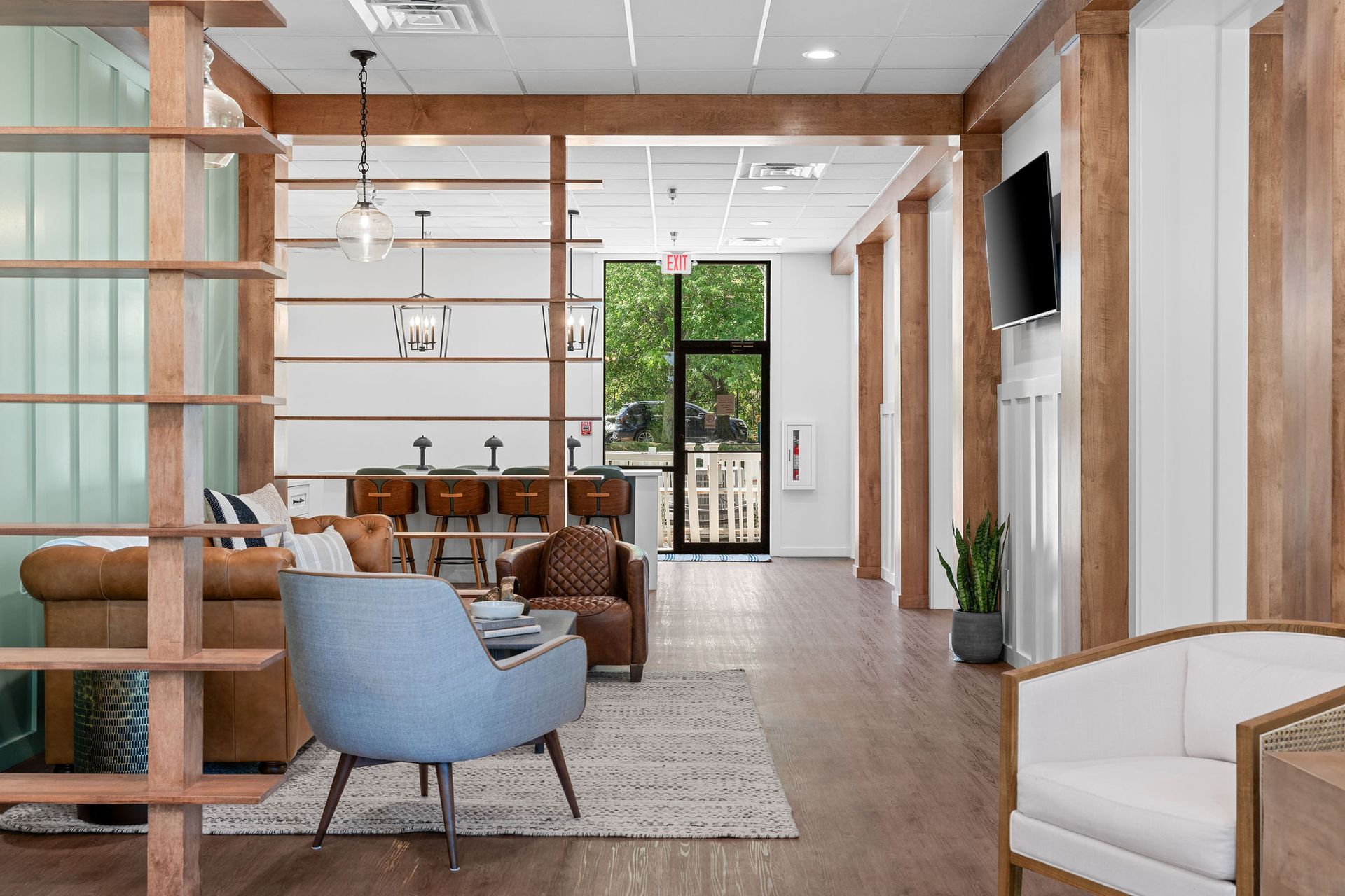 A modern, open-concept lobby with leather and upholstered seating, wooden accent pillars, and a glass door entrance.