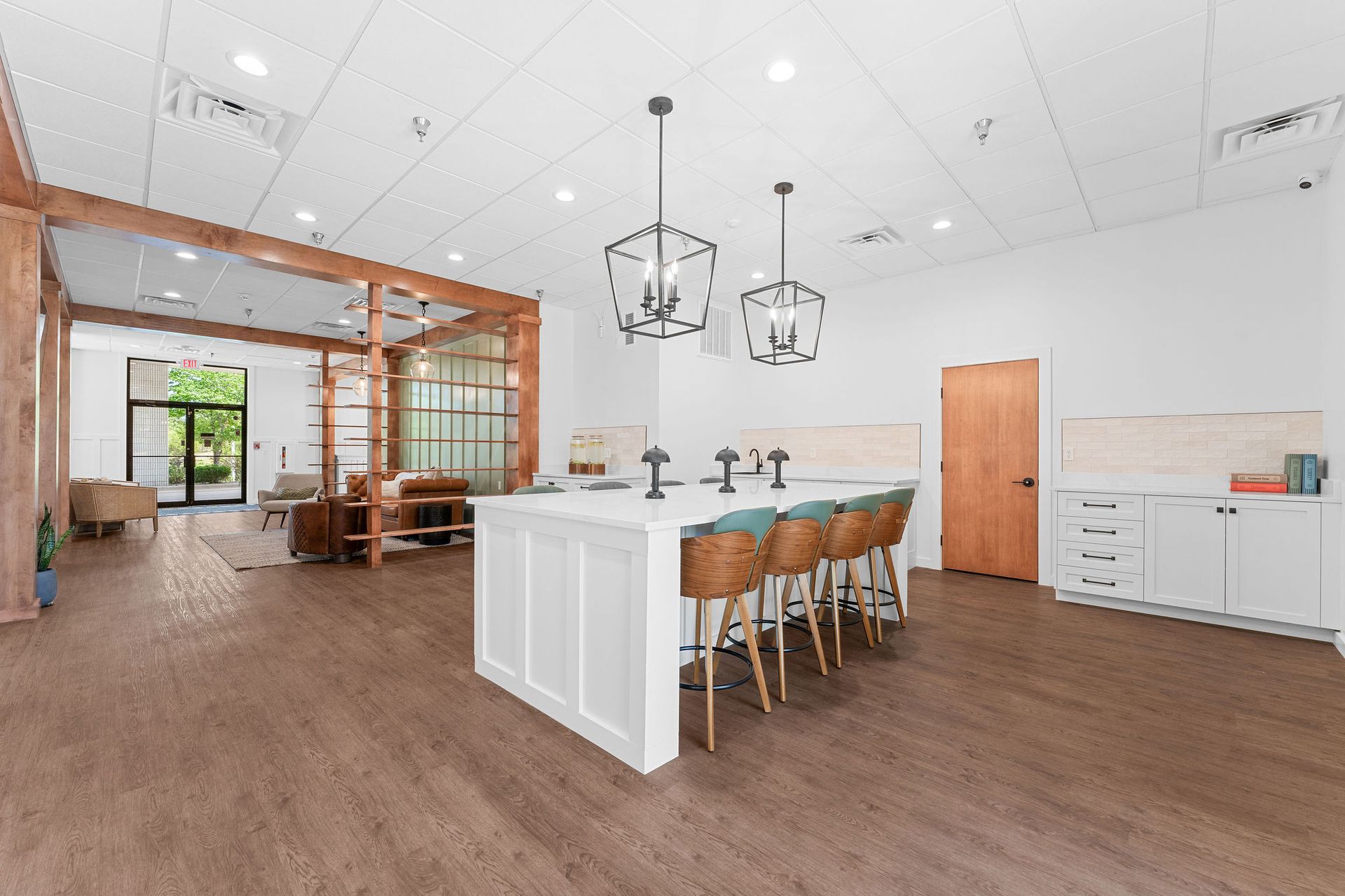 A bright, modern kitchen featuring a white center island with stools, hardwood floors, and wood-framed room dividers.