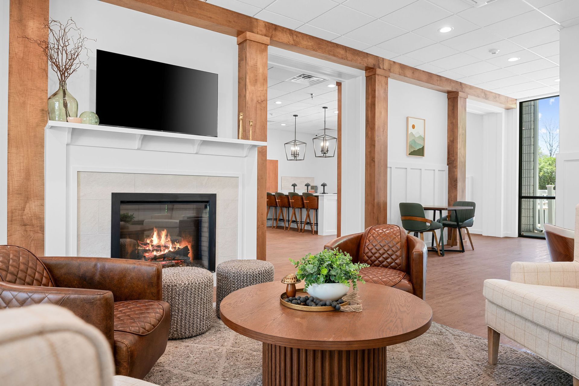A cozy lounge with a fireplace, leather armchairs, a wooden coffee table, and an adjacent room with a bar counter.