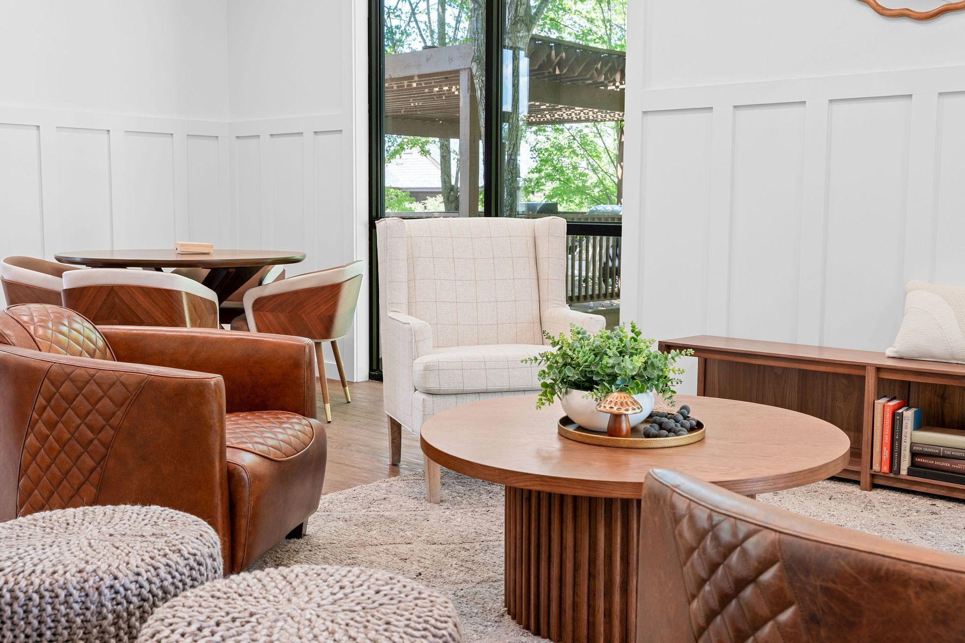 A cozy lounge area featuring leather armchairs, a white wingback chair, a round wooden coffee table, and a bookshelf.