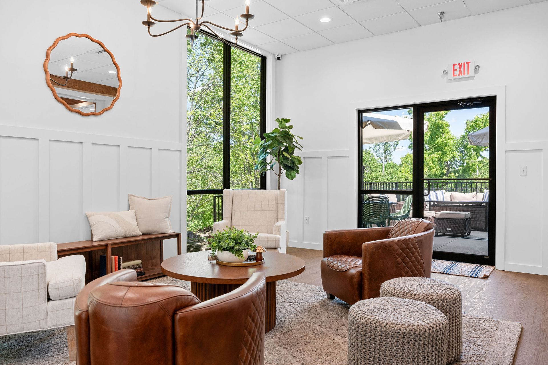 A bright lounge area with white walls, leather armchairs, a wooden coffee table, a tall window, and a patio door.