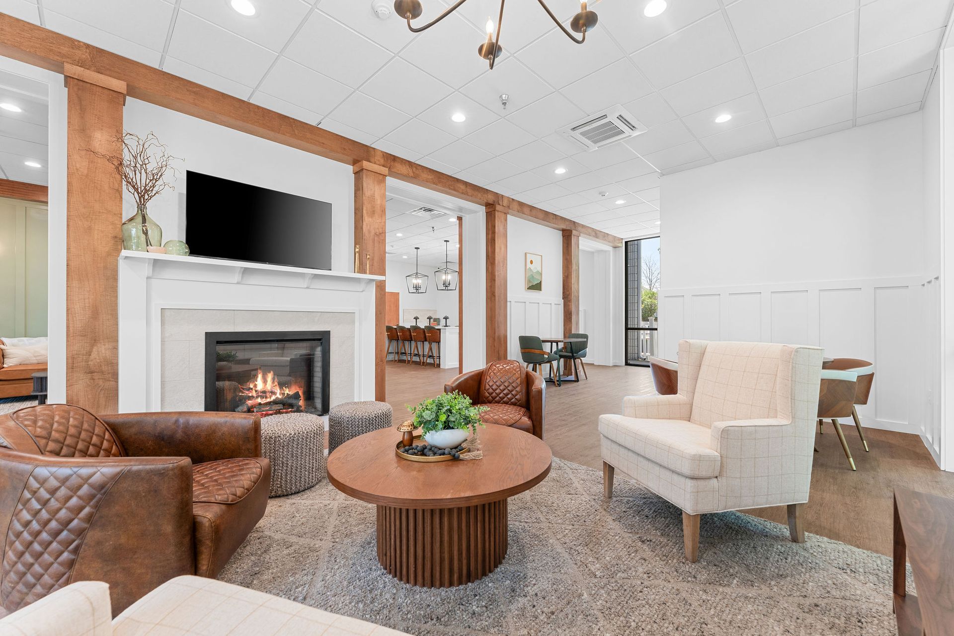 A cozy lounge featuring a fireplace with a mounted television, leather and upholstered seating, and a circular wood table.