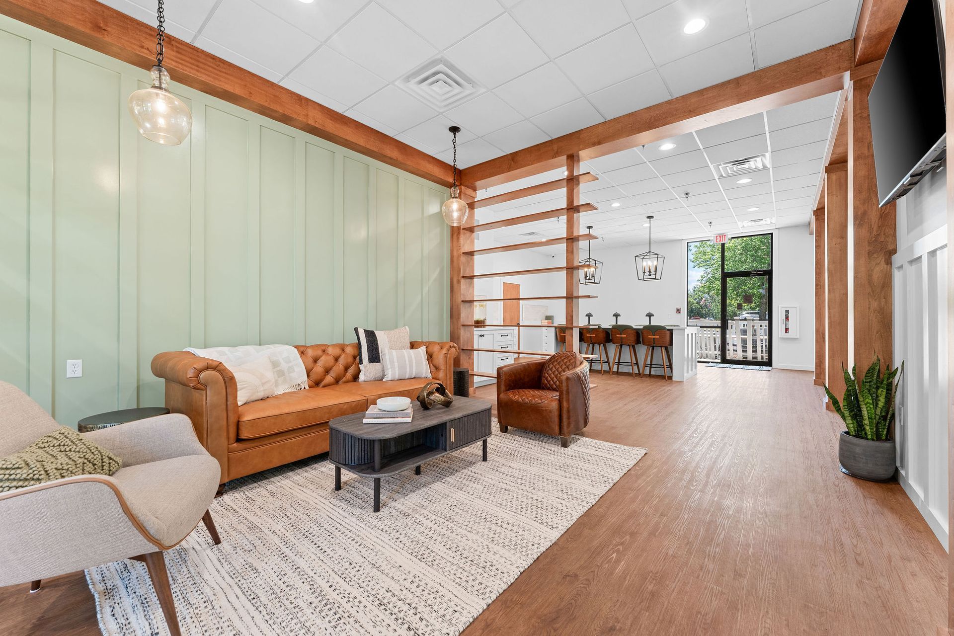 Modern lounge area with a tan tufted sofa, light-colored armchair, a coffee table, and wood-toned decor on a green wall.