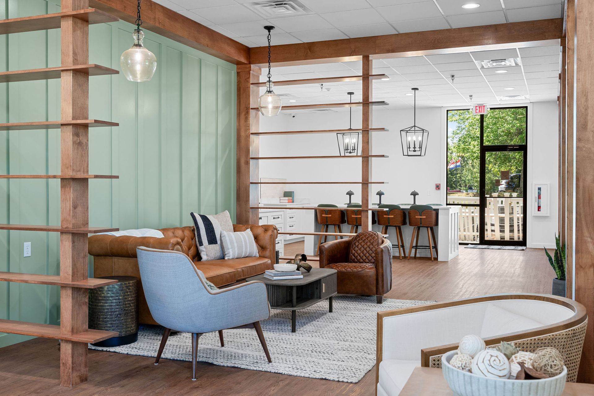 Modern lounge with sage green paneling, leather sofa, armchair, and open wooden shelving.