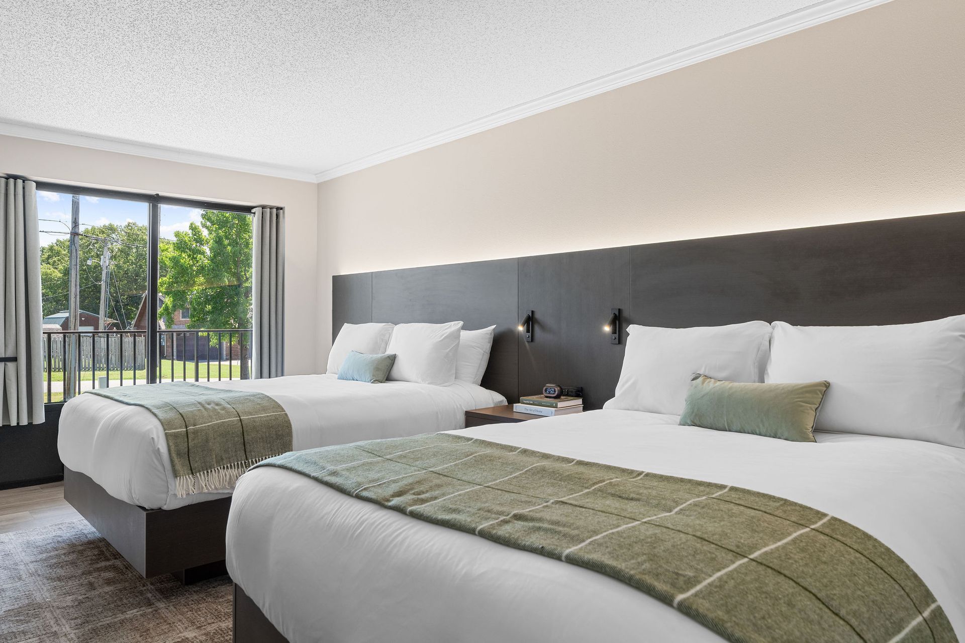A hotel room with two beds, featuring white linens, olive green patterned runners, and a dark wood headboard wall.
