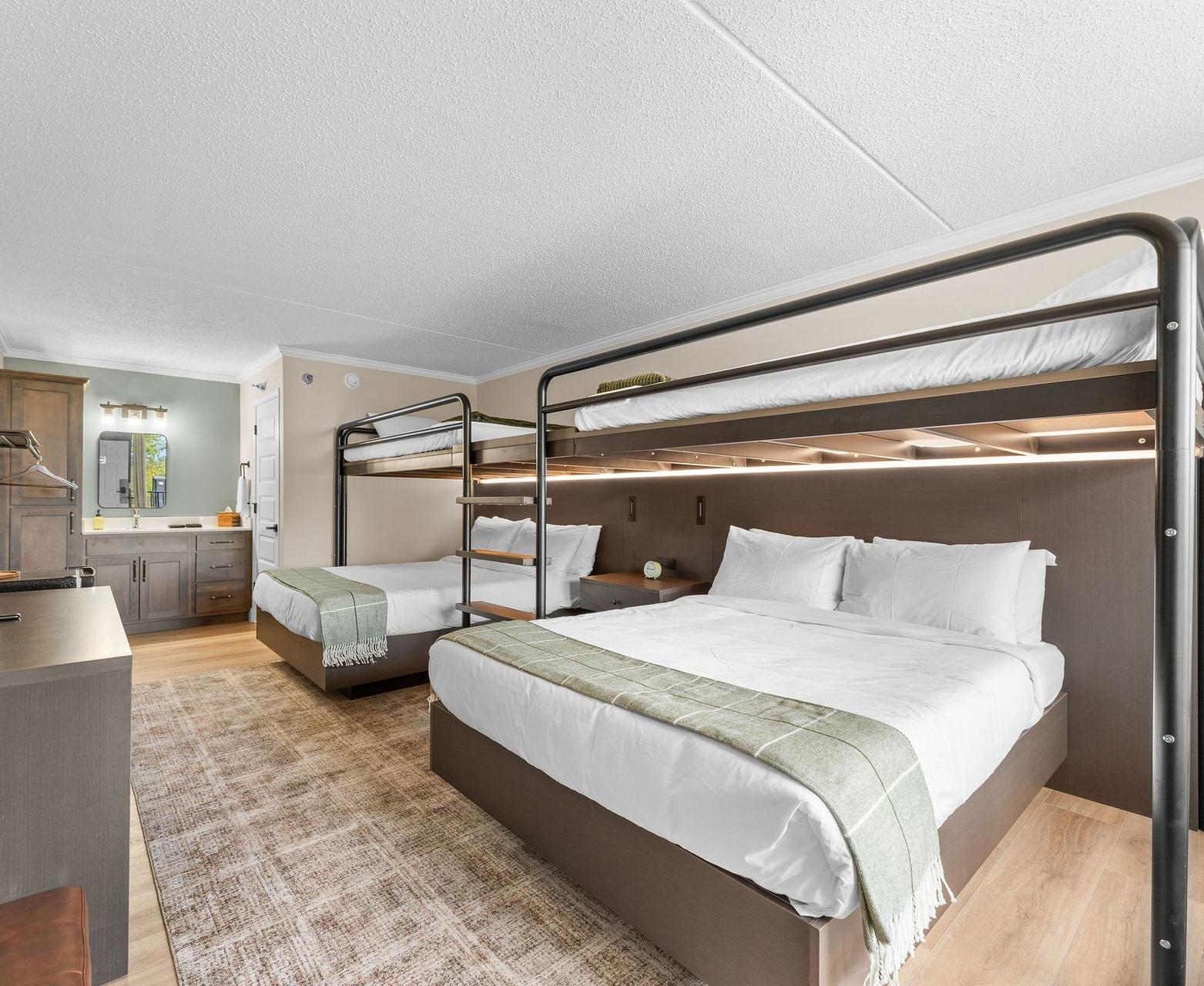 Hotel room with two sets of bunk beds featuring white linens and sage green runners on a light wood floor.