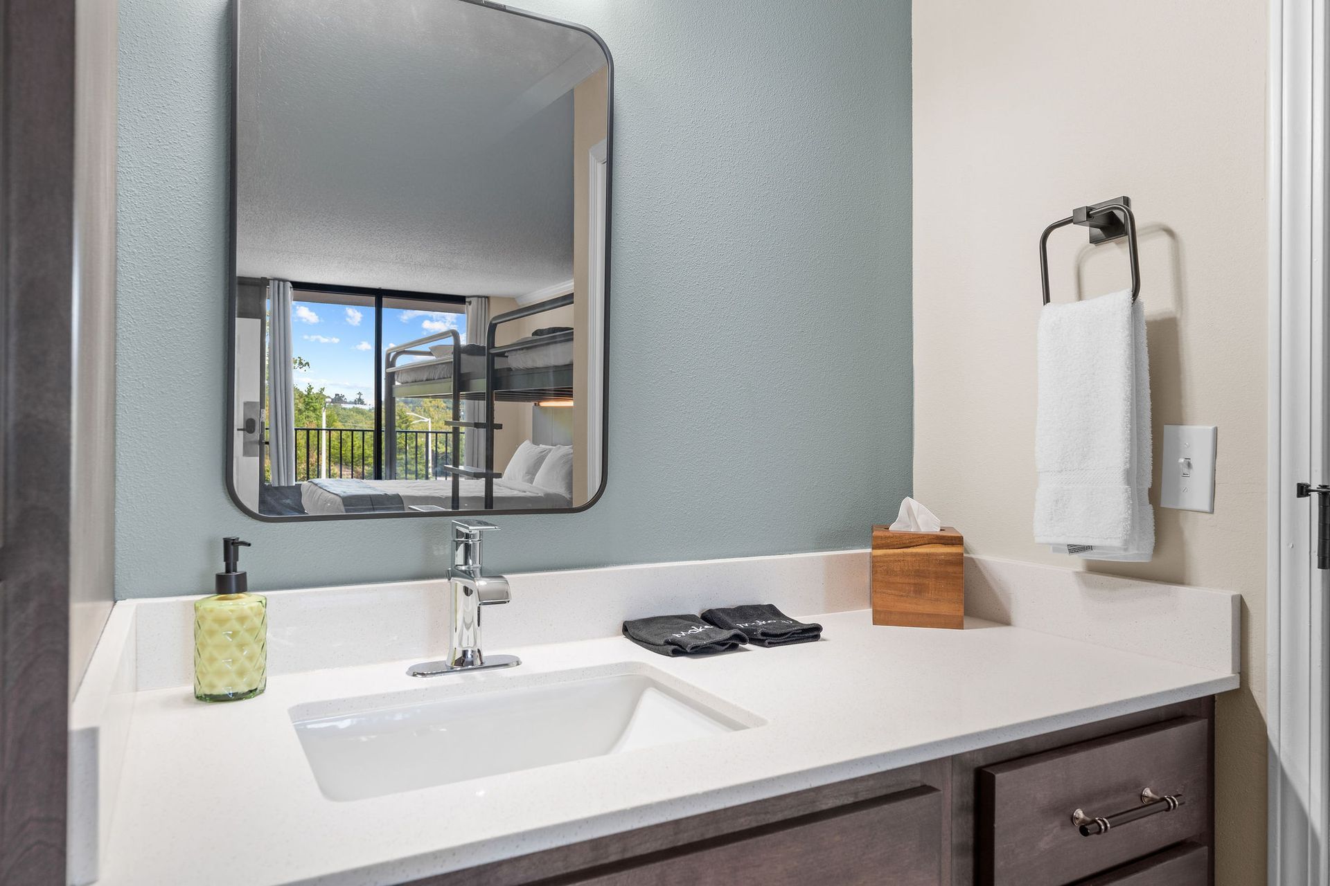 A bathroom vanity with a white countertop, sink, mirror, and towel hanging on the wall.