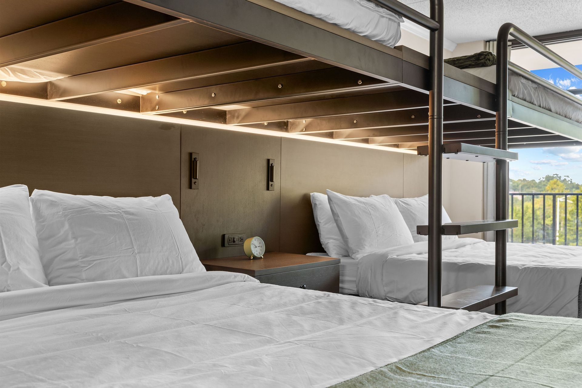 A hotel room featuring two beds, with a metal bunk bed frame structure over the lower beds.