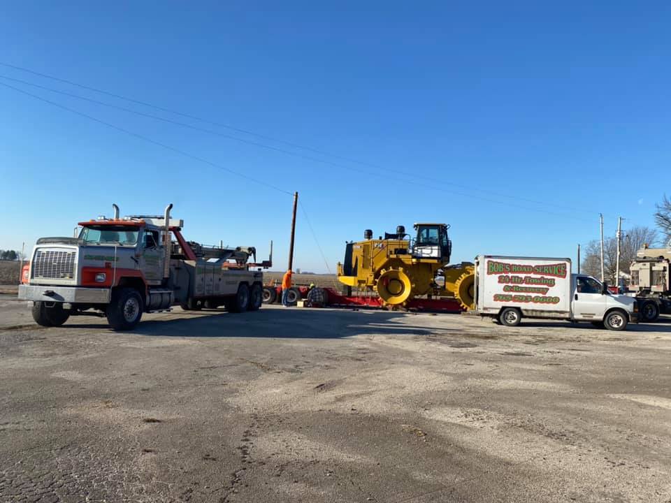 A tow truck is towing a bulldozer in a parking lot.