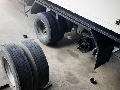 A truck with a broken wheel is being repaired in a garage.