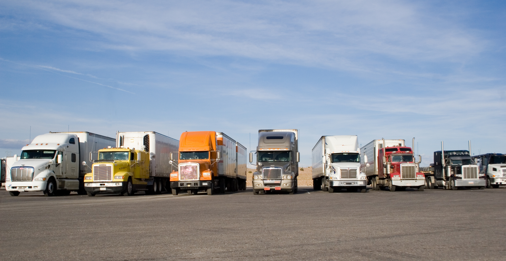 A row of semi trucks are parked in a parking lot
