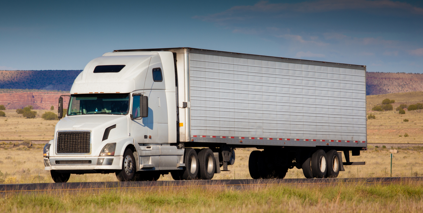 A semi truck is driving down a road in the middle of a field.