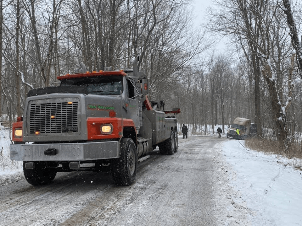 A tow truck is driving down a snowy road.