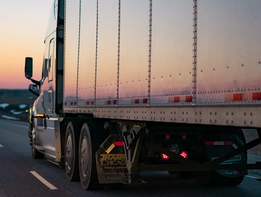 A semi truck is driving down a highway at sunset.