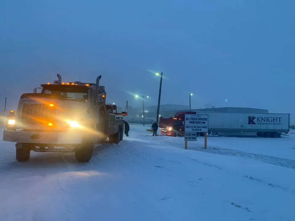 A truck is driving down a snowy road next to a building.