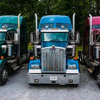 Three semi trucks are parked next to each other in a gravel lot.