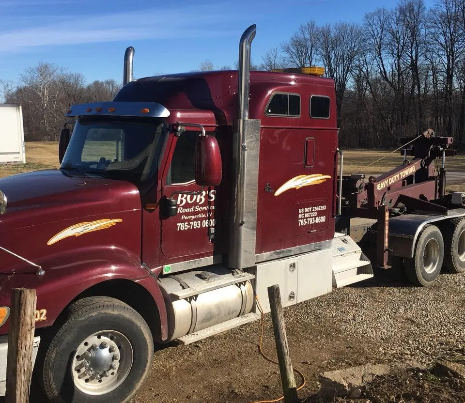 A red tow truck is parked in a gravel lot