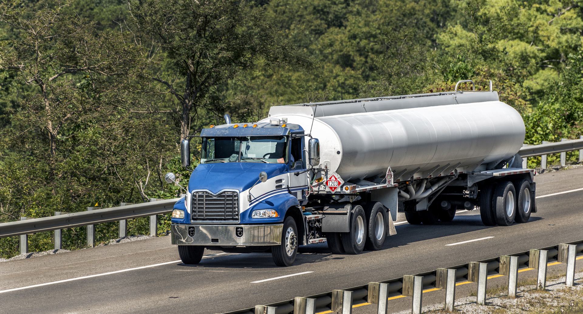 A blue and silver tanker truck is driving down a highway.