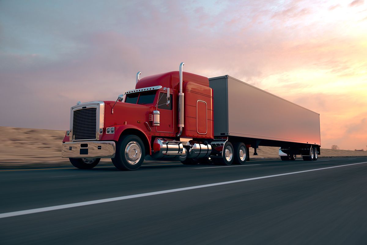 Red semi-truck driving on highway at sunset.