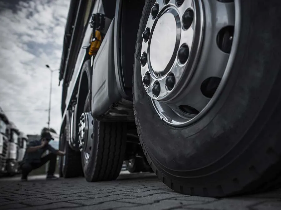 A man is squatting down next to a large truck.