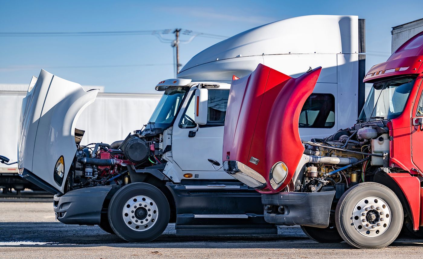Two semi-trucks parked outdoors with their hoods open for maintenance.