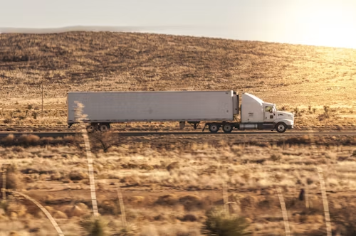 White semi-truck hauling a trailer through a dry, sunlit landscape