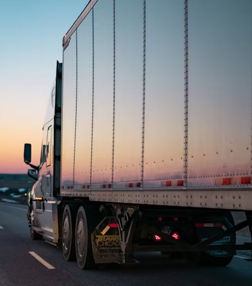 A semi truck is driving down a highway at sunset.