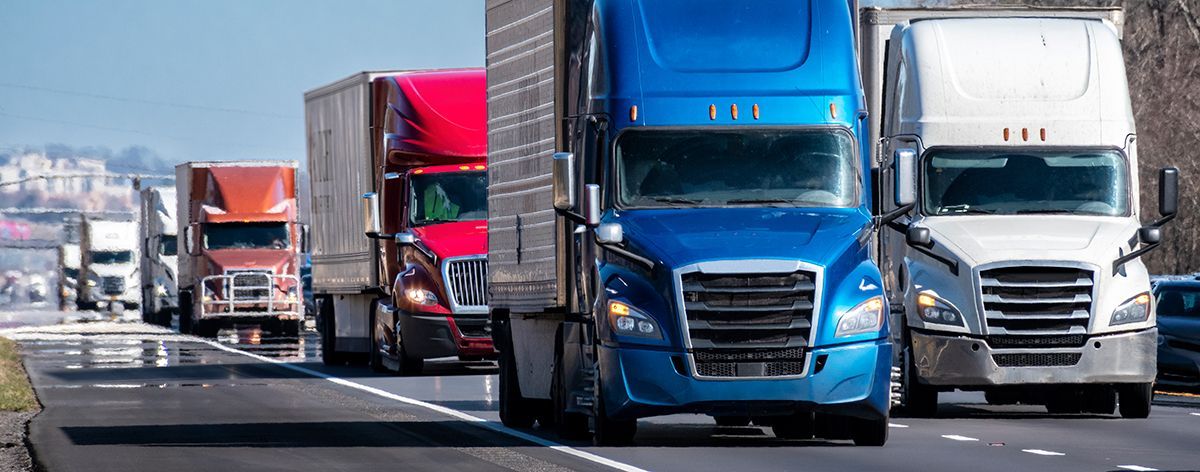 A row of semi trucks are driving down a highway.