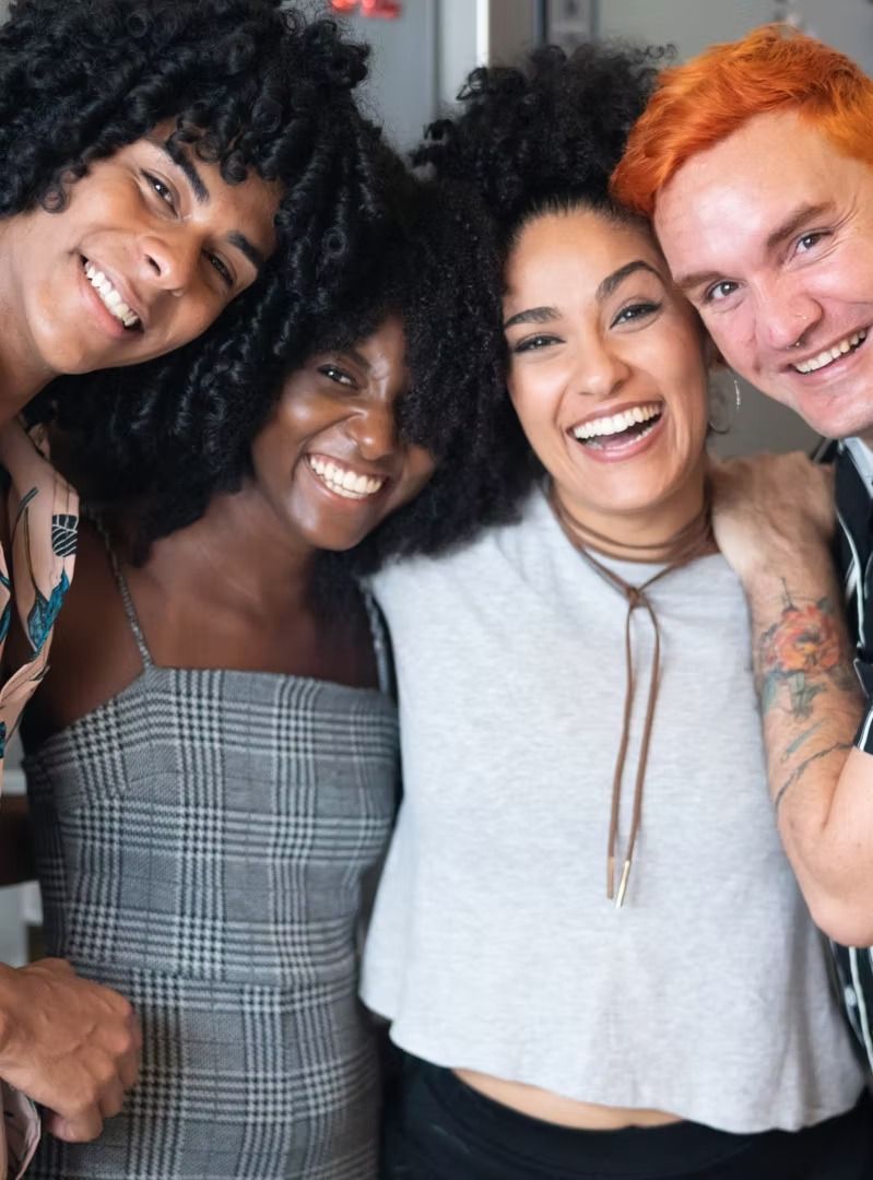 Four friends smiling closely together, posing in a casual indoor selfie