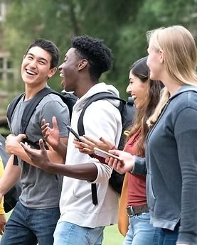 Four friends walking outdoors, smiling and talking, with phones in hand.