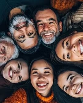 Smiling group of seven people lying in a circle, faces close together, looking up at the camera.