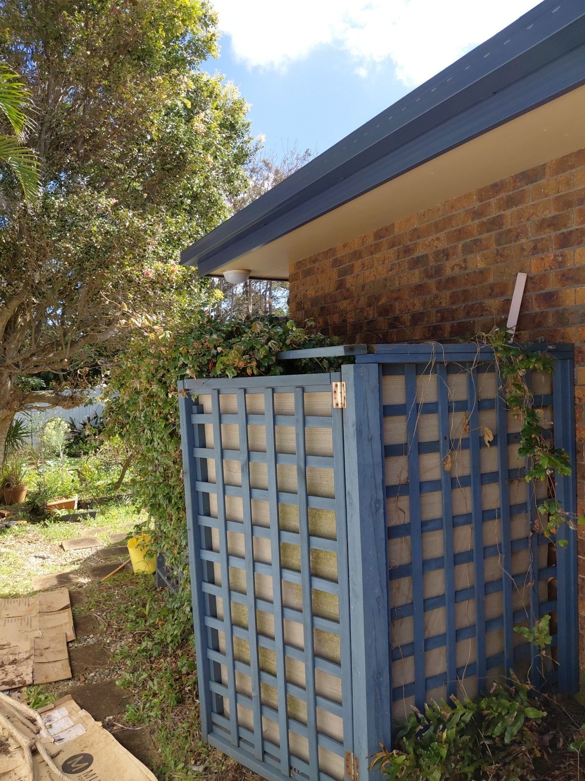 Partially built brick house with blue tarp and exposed roof under a bright sunny sky