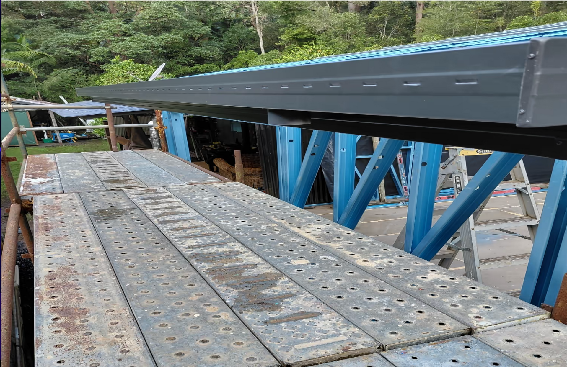 Blue steel truss bridge deck under construction with wooden planks and forested background