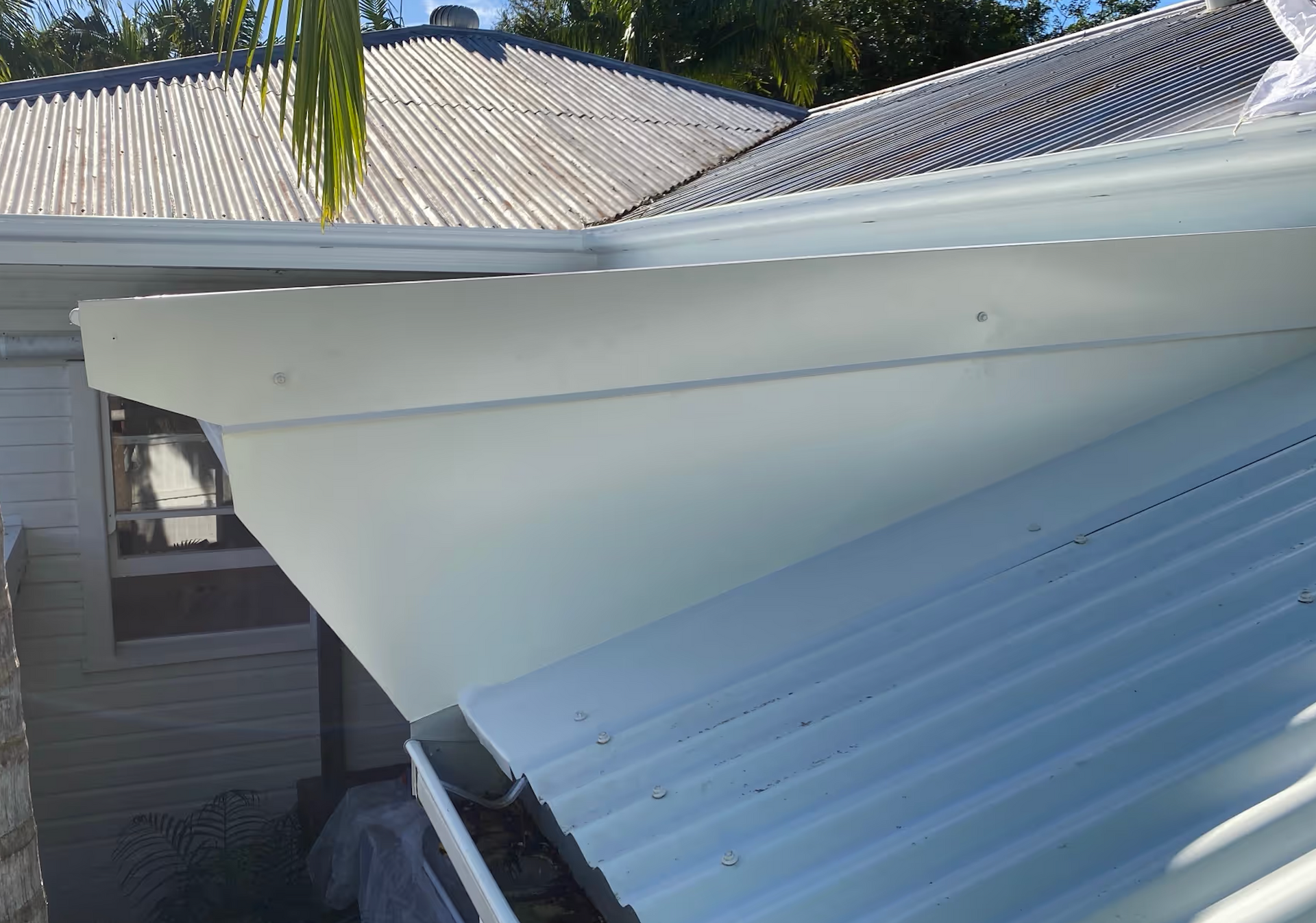 White corrugated metal awnings over a house roof, seen from above in bright sunlight
